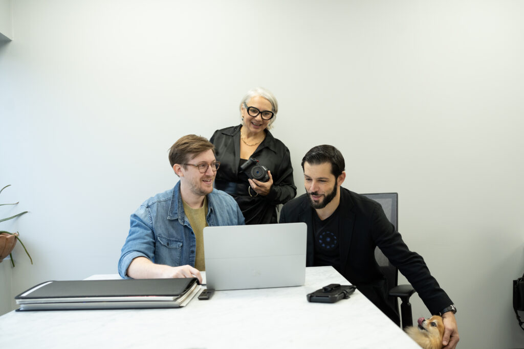 Alex Gambino, Carolina Luna, and Craig Escobar standing over laptop in office.